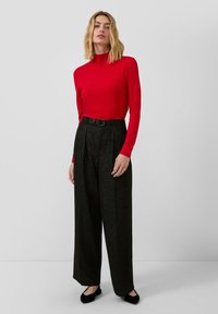 Rode lange mouw turtleneck top gecombineerd met high-waisted, wijde zwarte broek met een subtiele glans en een zwarte riem. Zwarte flats maken de outfit compleet.