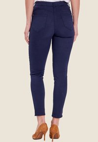 Jeans skinny blu navy con vita media, dotati di tasche posteriori e una texture liscia. Abbinati a scarpe col tacco alte color cammello.