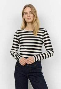 Maglietta a maniche lunghe a righe bianche e nere con scollatura rotonda, realizzata in un tessuto testurizzato, indossata con jeans blu scuro.