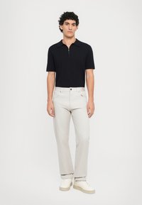 Zwarte rits-polo, lichtgrijze broek en witte sneakers. Slim fit, katoenmix, gladde textuur, minimalistisch ontwerp, geen patronen.