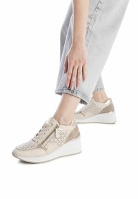 Sneakers beige con design perforato, dettagli metallici e suola a cuneo bianca imbottita. Presentano una chiusura con cerniera e lacci.