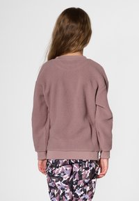 Brown fleece sweatshirt with a textured finish, crew neck, and ribbed cuffs, paired with patterned pants in shades of purple and pink.