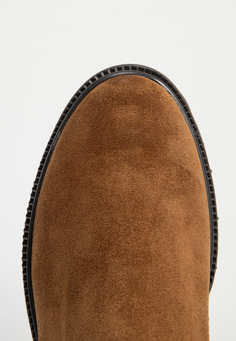 Braune Wildleder-Ankle Boots mit runder Spitze und strukturiertem Obermaterial, ausgestattet mit einer schwarzen Gummisohle und dezenten Nähten entlang der Kante.
