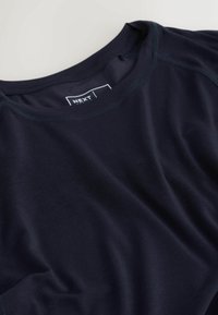 Tengerészkék kerek nyakú póló puha anyagból, finom varrási részletekkel. A logócímke látható a nyakkivágás belső részén.