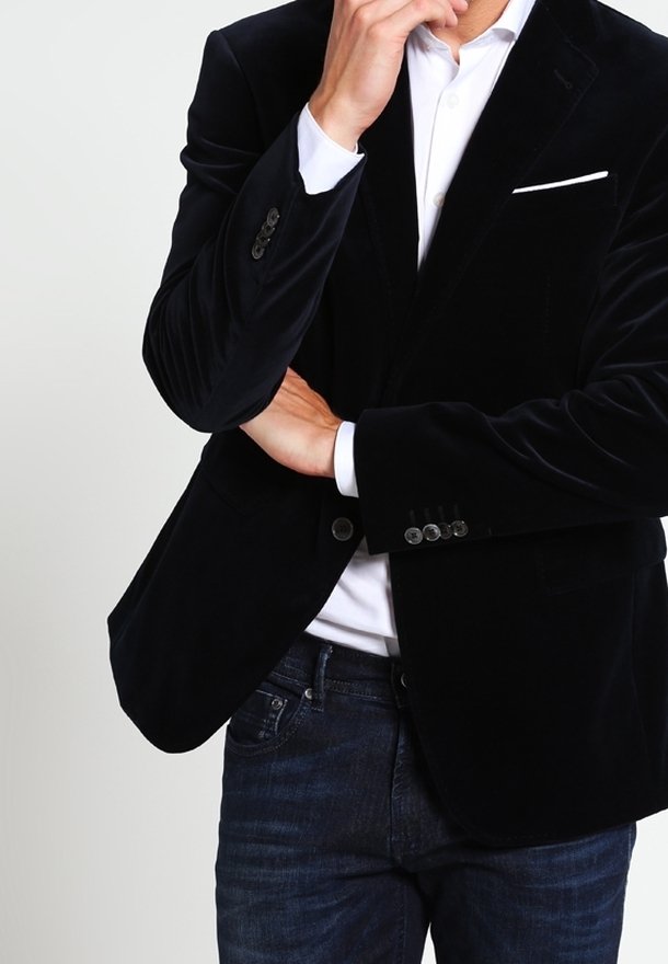 Svart sammet blazer med snedskuren slag, enkel vit fickduk och silverknapp detaljer, matchat med mörka denimjeans och en vit skjorta.