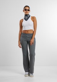 Vit kortärmad crop-top, grå utsvängda byxor, mönstrad halsduk, solglasögon. Tyget verkar mjukt med en figurnära design för toppen och lös passform för byxorna.