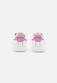 White sneakers with pink accents, featuring a smooth leather finish, rounded shape, padded collar, and distinctive logo at the heel.