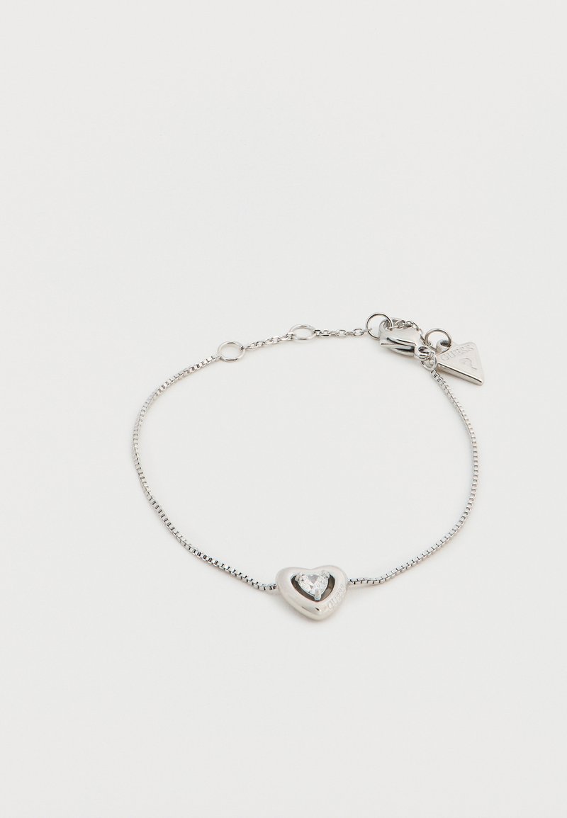 Ασημένιο βραχιόλι με μενταγιόν σε σχήμα καρδιάς, που διαθέτει ένα διαυγές κρύσταλλο στο κέντρο του, προσαρτημένο με λεπτή αλυσίδα και μικρή ετικέτα λογότυπου.