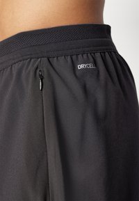 Los pantalones cortos deportivos negros cuentan con una cinturilla elástica texturizada, un pequeño bolsillo con cremallera y un logo "DRYCELL" en blanco. Tejido suave y ligero.