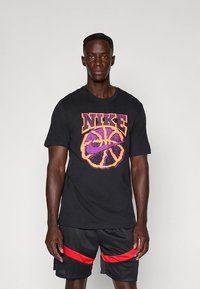 Mustast puuvillast T-särk, millel on suur lilla ja oranž korvpalligraafik ning "NIKE" tekst. Kantakse koos mustade lühikeste pükstega, millel on punased triibud.