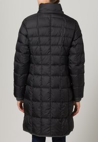 Zwarte pufferjas met een gewatteerd patroon, hoge kraag en lange mouwen. Het materiaal lijkt glanzend en heeft geribde manchetten en een middellange snit.