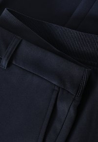 Gros plan de deux ceintures de pantalon noires, l'une élastique côtelée et l'autre avec une boucle de ceinture et une texture de tissu lisse.