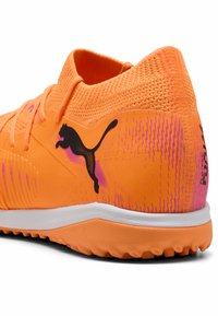Lys orange atletisk sko med en tekstureret overdel, sort logo og rosa accenter. Har en polstret sål og et tætsiddende kravedesign.