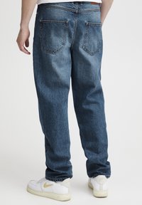 Zilas džinsa bikses ar taisnu kāju griezumu, piecām kabatām un izbalējušām vietām. Kombinētas ar baltām sporta kurpēm ar zelta akcentu.