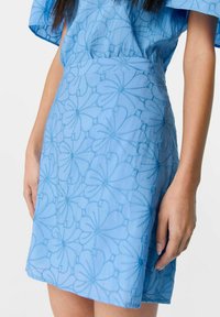 Vestido azul claro con bordado floral, silueta ajustada y dobladillo corto. Está hecho de una tela texturizada con un acabado suave.