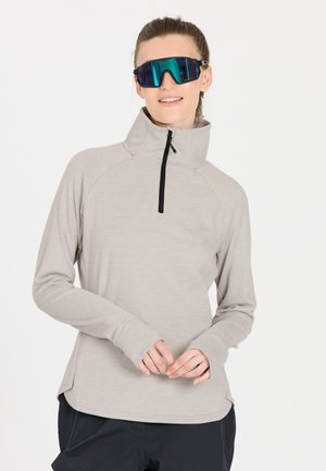 Light gray half-zip long-sleeve shirt with a high collar and soft texture, paired with large blue-tinted sunglasses. Black pants visible.