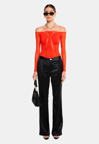 Röd off-shoulder bodysuit med strukturerad design, matchad med svarta, högmidjade satinträningsbyxor och en liten svart handväska.