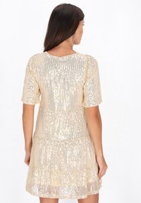 Rochie scurtă, de culoare aurie, din mărgele cu paiete, cu mâneci scurte, tiv în straturi și spate în formă de V, având o textură și un model strălucitor.