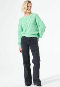Pull en tricot vert menthe avec un motif de diamant texturé, associé à un jean noir évasé avec des éclats clairs. Manches longues et poignets côtelés.