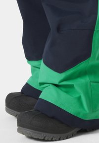 Zelené a námořnické voděodolné kalhoty mají uvolněný střih, strukturální látku a zpevněnou černou obuv s robustní podrážkou.