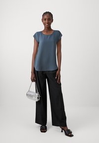 Dark blue top with cap sleeves, paired with black wide-leg pants. Silver purse with chain strap. Black heeled mules feature a large buckle.
