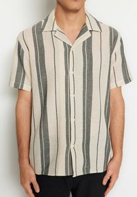 Korte mouw shirt in lichtbeige met verticale donkergrijze strepen, met een kraag en knoopsluiting aan de voorkant. Textuurstof.