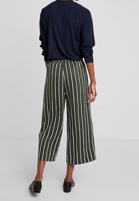 Gröna och vita randiga vida byxor i kombination med en marinblå långärmad topp. Har en elastisk midja och en slät tygstruktur.