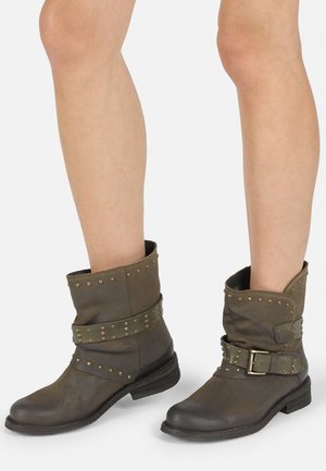 Braune Lederstiefel bis zum Knöchel mit umgeschlagenem Schaft, Nietenakzenten und einer breiten Schnalle. Mit einem niedrigen, gestapelten Absatz und glatter Oberfläche.