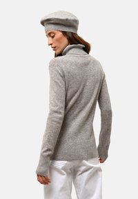 Šedý rolák se strukturovaným povrchem a žebrovanými manžetami, doplněný o ladící baret, zobrazený zezadu na jednobarevném pozadí.