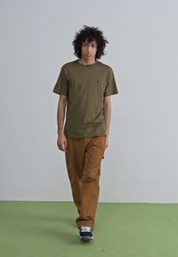 Olive green short-sleeve t-shirt, brown pants, and black shoes. Simple design with a small logo on the shirt. Smooth fabric texture.