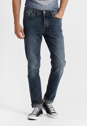Donkerblauwe denim jeans met een recht model, vijf zakken en een ritssluiting, gedragen met zwarte hoge sneakers.