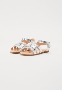 Silver glittrande sandaler med en remdesign, öppen tå och justerbar vristrem på en ljusbrun sula.