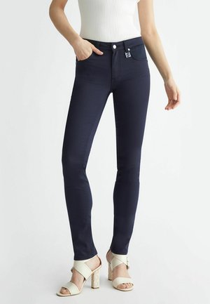 Jeans skinny blu navy realizzati in cotone elasticizzato. Presentano quattro tasche e una chiusura frontale con bottone. Abbinati a sandali con tacco color crema.