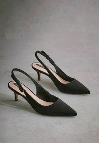 Mustat mokkanahasta valmistetut slingback-kengät, joissa on terävät kärjet, hoikat korot ja nauha yksityiskohtana takana. Silkkinen sisävuori.