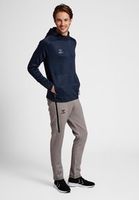 Granatowa bluza z kapturem z czarnymi akcentami i logo; jasnoszare dresy z dekoracyjnym szwem i czarnymi paskami; sportowe czarne buty.