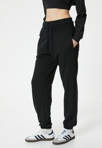 Zwarte sweatpants van zacht materiaal, met een elastische tailleband en zijzakken, taps toelopende boorden en een ontspannen pasvorm. Gecombineerd met witte sneakers.
