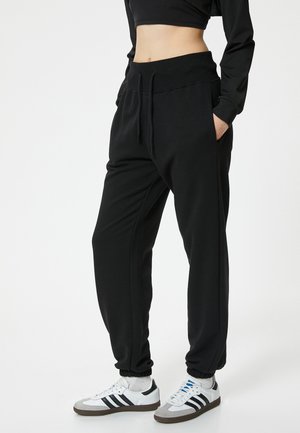 Schwarze Jogginghosen aus weichem Material, mit einem elastischen Bund und Seitentaschen, tapered Cuffs und einem lockeren Schnitt. Kombiniert mit weißen Sneakern.
