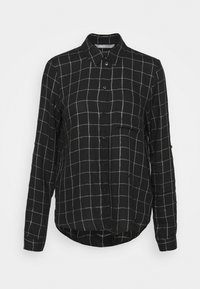 Chemise noire à manches longues présentant un motif à carreaux avec des lignes blanches, boutonnage à l'avant, col pointu, et une poche poitrine unique. Tissu doux.