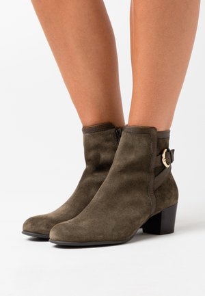 Olivgrüne Wildleder-Stiefeletten mit einer runden Zehenpartie, seitlichem Reißverschluss und einer dekorativen Schnalle. Sie verfügen über einen Blockabsatz für zusätzliche Stabilität.