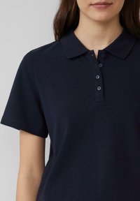 Granatowa koszulka polo wykonana z teksturowanej tkaniny, z klasycznym kołnierzykiem, posiadająca zapięcie na trzy guziki i krótkie rękawy.
