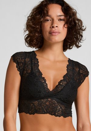 Zwarte kanten bralette met een diepe V-hals, geschulpte randen en kapmouwen. Het ingewikkelde bloemenpatroon heeft een zachte, sheer textuur.