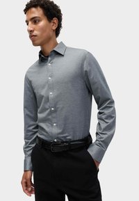 Grijze lange mouwen knoopshirt met een kraag en witte knopen, gecombineerd met zwarte broek en een zwarte riem. Glad stoffen textuur.