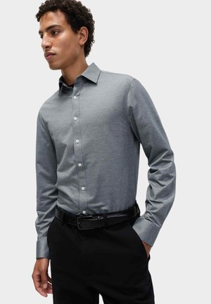 Grijze lange mouwen knoopshirt met een kraag en witte knopen, gecombineerd met zwarte broek en een zwarte riem. Glad stoffen textuur.