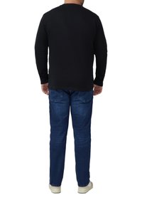 Czarna koszula z długim rękawem, niebieskie dżinsy i białe trampki, widziane od tyłu. Prosty wzór bez widocznych wzorów ani akcentów.