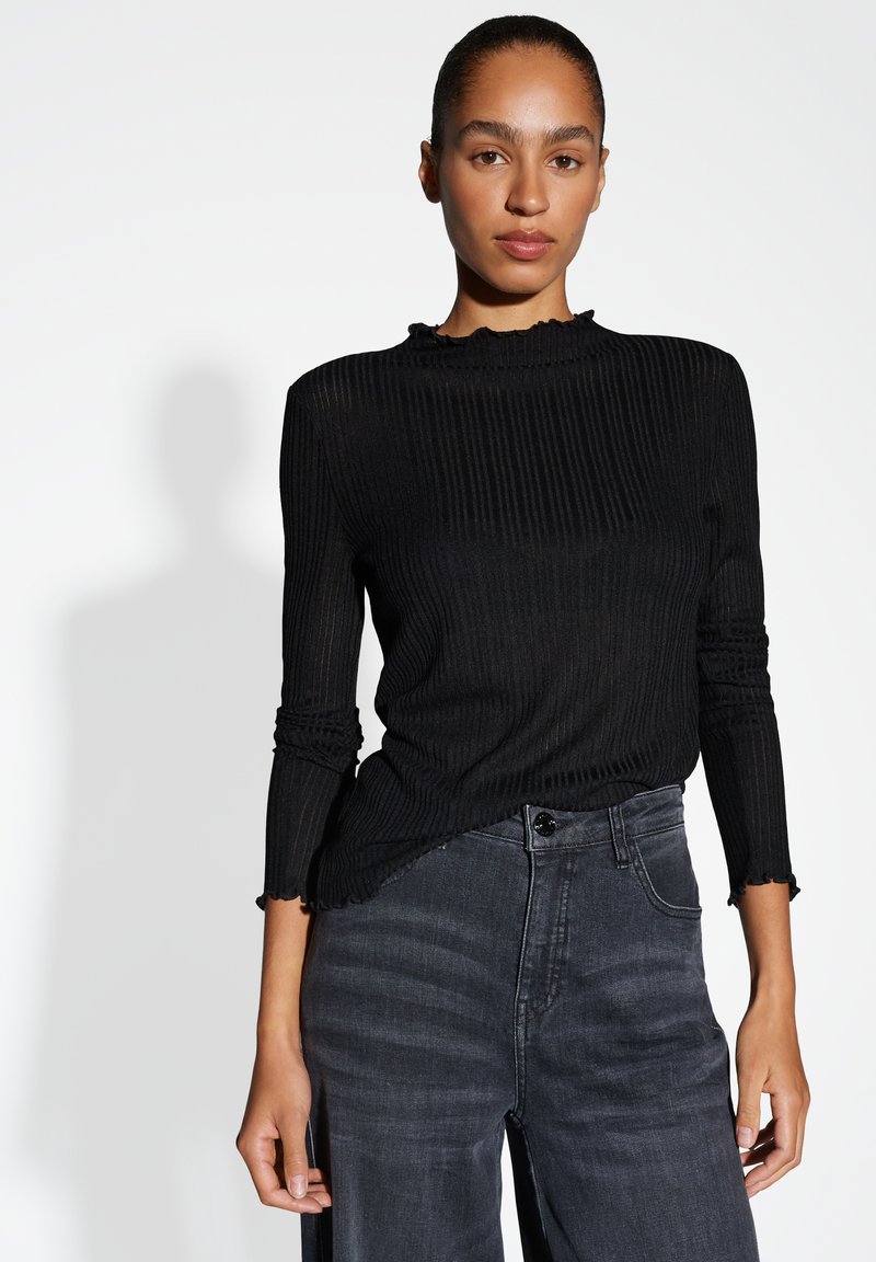 Schwarzes geripptes Longsleeve-Top mit hohem Kragen und rüschensaum, kombiniert mit dunkelgrauen weiten Jeans mit Knopfverschluss.