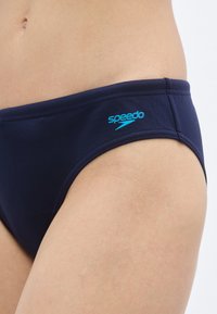 Μαγιό Speedo τύπου σλιπ σε ναυτικό μπλε ύφασμα, με άνετη μέση και ανοιχτό μπλε λογότυπο Speedo στο πλάι.