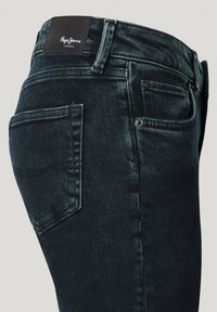 Jeans de mezclilla oscura con una textura suave, que presentan un diseño clásico de cinco bolsillos y un parche de cuero en la cinturilla.