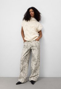 Kremowy, dzianinowy top z wysokim dekoltem, w zestawie z szerokimi, szarymi spodniami w marmurkowy wzór oraz czarnymi, spiczastymi butami. Gładka tekstura z widocznymi wzorami.