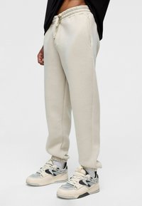 Beige katoenen sweatpants met een elastische tailleband met trekkoord, zijzakken en een ontspannen pasvorm, gecombineerd met chunky sneakers.