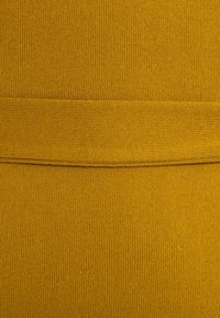 Tissu tricoté dans une riche couleur jaune moutarde, présentant une texture lisse et un détail de bande horizontale au centre.